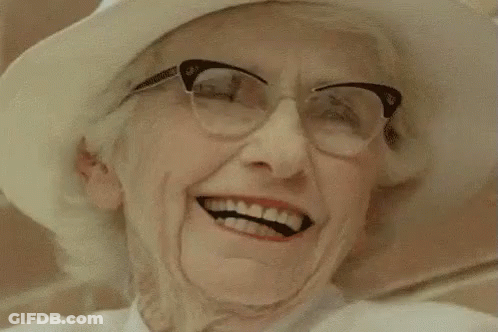 An Older Woman Wearing Glasses And A White Hat Is Smiling . GIF