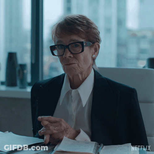 An Older Woman Wearing Glasses Sits At A Desk With A Netflix Logo On The Bottom Right GIF