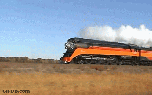 An Orange And Black Train Is Going Down A Track GIF