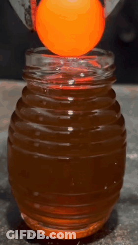 An Orange Ball Is Being Held Over A Jar Of Liquid GIF