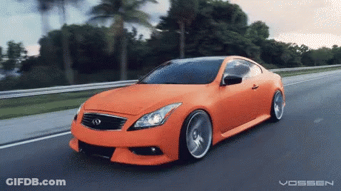 An Orange Car Is Driving Down A Road With The Word Vossen On The Bottom Right GIF