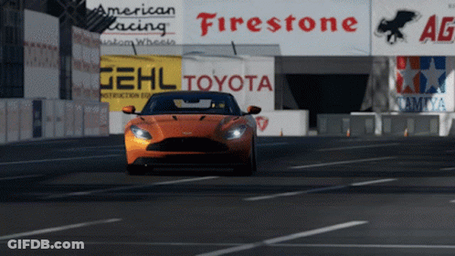 An Orange Sports Car Is Driving Down A Road In Front Of A Sign That Says Toyota GIF