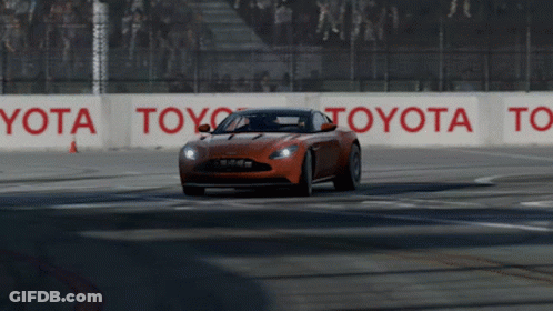 An Orange Sports Car Is Driving On A Race Track With Toyota Signs On The Side GIF
