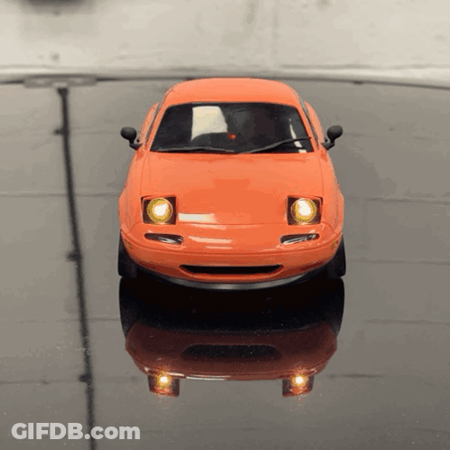 An Orange Toy Car Is Sitting On A Black Table GIF