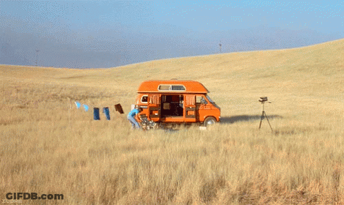 An Orange Van Is Parked In The Middle Of A Field With Clothes Hanging On A Line GIF