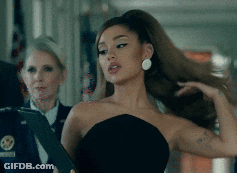 Ariana Grande In A Black Strapless Dress Is Holding A Clipboard GIF