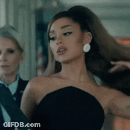 Ariana Grande Is Wearing A Black Strapless Dress And Earrings While Standing Next To A Woman . GIF