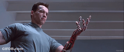 Arnold Schwarzenegger Is Holding A Bloody Robotic Arm In A Scene From Terminator GIF
