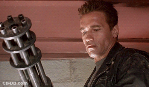 Arnold Schwarzenegger Is Holding A Machine Gun In His Hand GIF