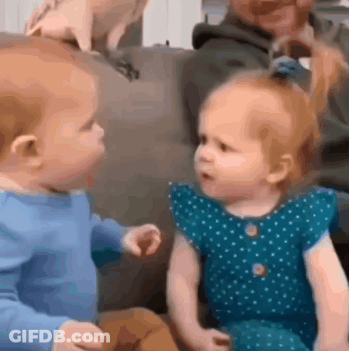 Baby And Little Girl Sitting On Couch Looking At Each Other GIF