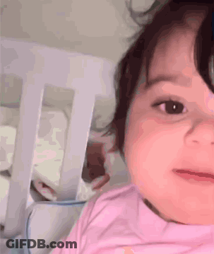 Baby Girl In Pink Shirt Laying In Crib Looking At Camera GIF