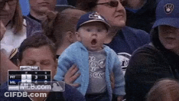 Baby In Baseball Cap Held By Woman In Crowd GIF