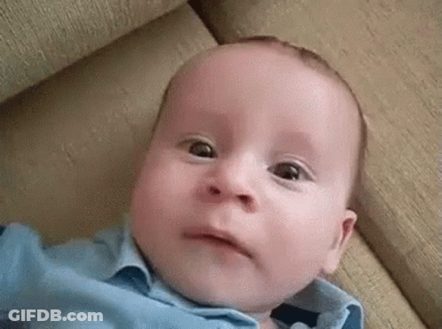 Baby In Blue Shirt Making Funny Face On Couch GIF