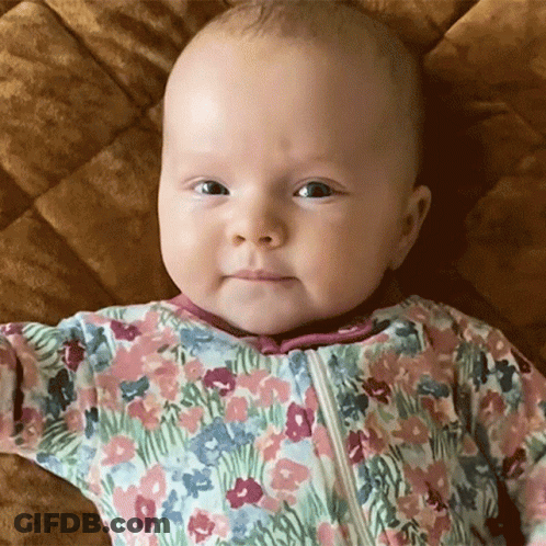 Baby In Floral Outfit Laying On Bed GIF