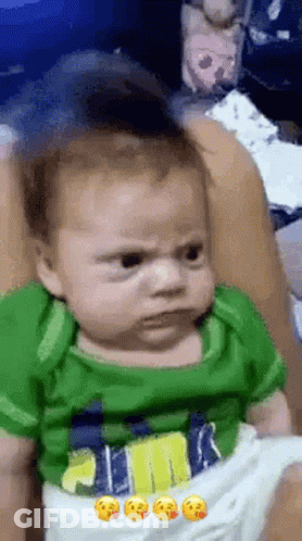 Baby In Green Shirt Making Funny Face On Bed GIF