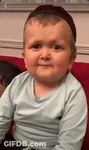 Baby In Hat And Blue Shirt Sitting On Couch GIF