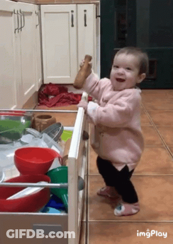 Baby In Pink Coat Standing In Kitchen Drawer Holding Salt Shaker GIF