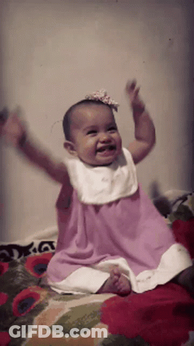Baby In Pink Dress Sitting On Bed GIF