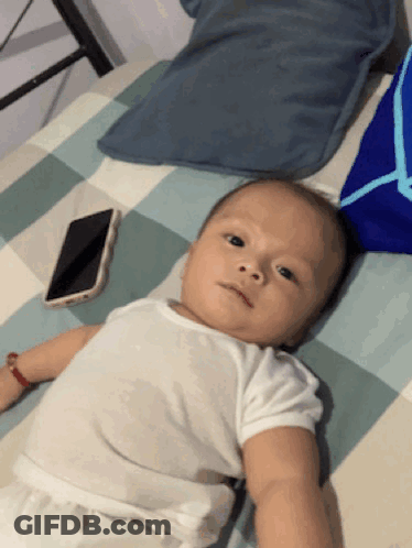 Baby Lying On Bed Next To Cellphone GIF