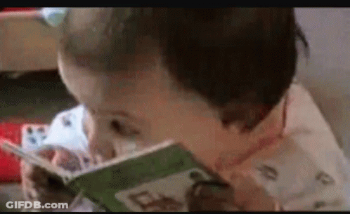Baby Reading Book With Spoon In Mouth GIF