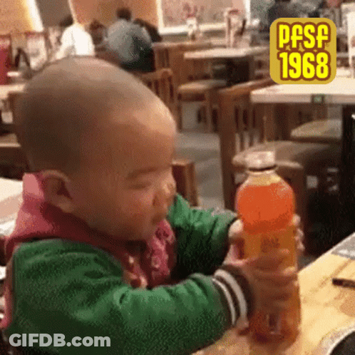 Baby Sitting At Table Holding Orange Soda GIF
