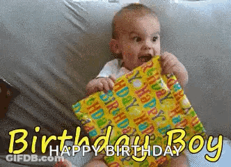 Baby Sitting On Bed Holding Birthday Present Says Happy Birthday GIF