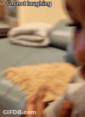 Baby Sitting On Bed Saying I'm Not Laughing GIF