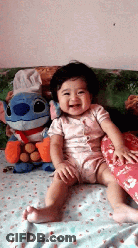 Baby Sitting On Bed With Stitch Stuffed Animal GIF