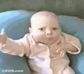Baby Sitting On Blue Pillow With Arms Outstretched GIF