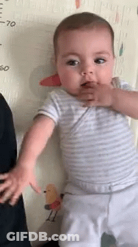 Baby Standing In Front Of Measuring Tape Looking At Camera GIF