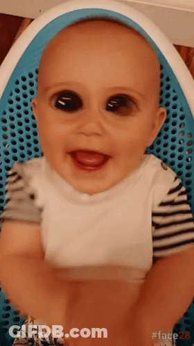 Baby With Big Black Eyes Sitting In Blue Chair Smiling GIF