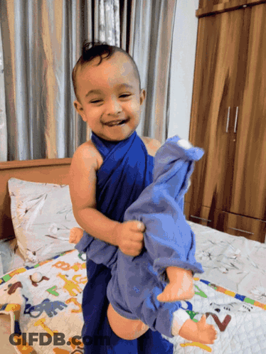 Baby Wrapped In Blue Holding Doll GIF