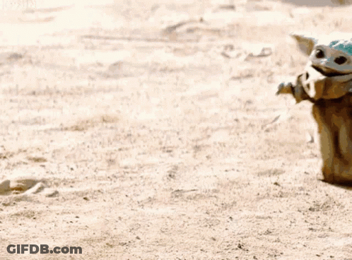 Baby Yoda Sitting On Sandy Beach Next To Person GIF