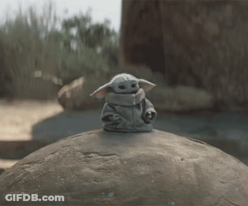 Baby Yoda Toy Sitting On Large Rock GIF
