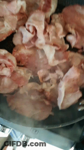 Bacon Is Being Cooked In A Pan With A Knife GIF