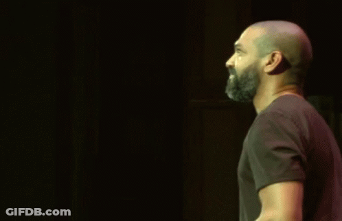 Bald Bearded Man Raising Hand In Dark GIF