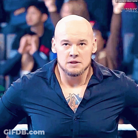 Bald Bearded Man With Chest Tattoo Facing Crowd In Boxing Ring GIF