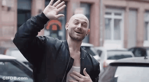 Bald Man In Black Jacket Waving And Smiling GIF