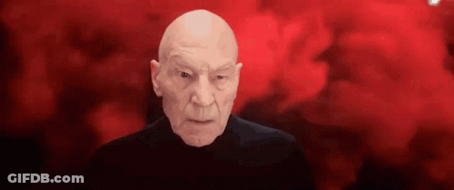 Bald Man In Black Shirt Looking At Camera GIF