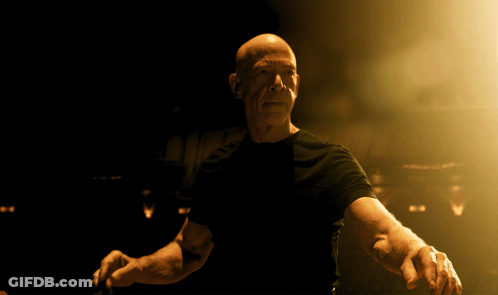 Bald Man In Black Shirt Standing In Dark Room GIF