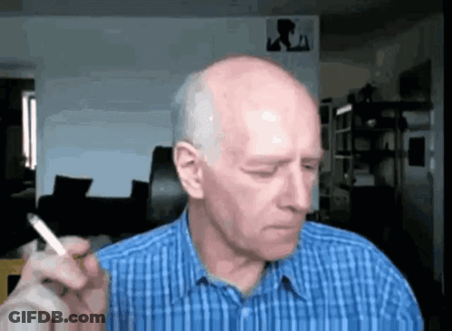 Bald Man In Blue Plaid Shirt Smoking Cigarette In Living Room GIF
