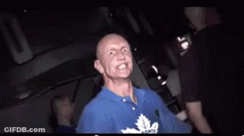Bald Man In Blue Shirt With Maple Leafs Sitting In Dark Room GIF