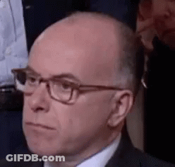 Bald Man In Glasses And Suit Sitting In Crowd GIF