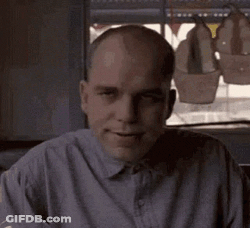 Bald Man In Gray Shirt Sitting By Window GIF