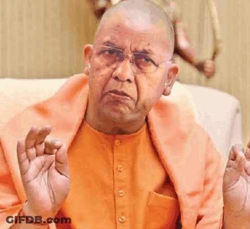 Bald Man In Orange Shirt And Glasses Sitting On Couch GIF