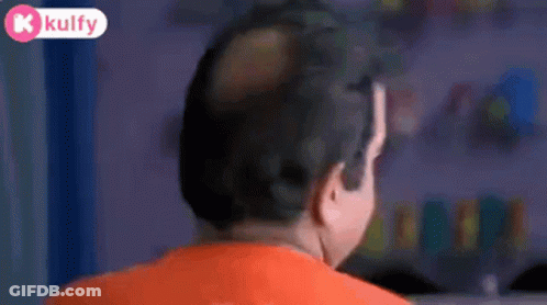 Bald Man In Orange Shirt Looking At Camera GIF