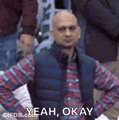 Bald Man In Plaid Shirt And Vest Sitting In Crowd GIF