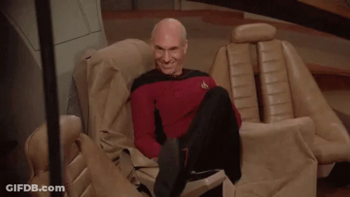 Bald Man In Red Shirt Sitting With Feet Up GIF