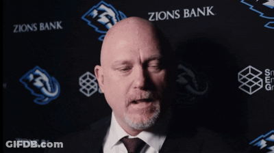 Bald Man In Suit And Tie In Front Of Zions Bank Banner GIF