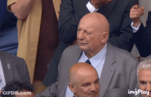 Bald Man In Suit And Tie Sitting In Crowd GIF